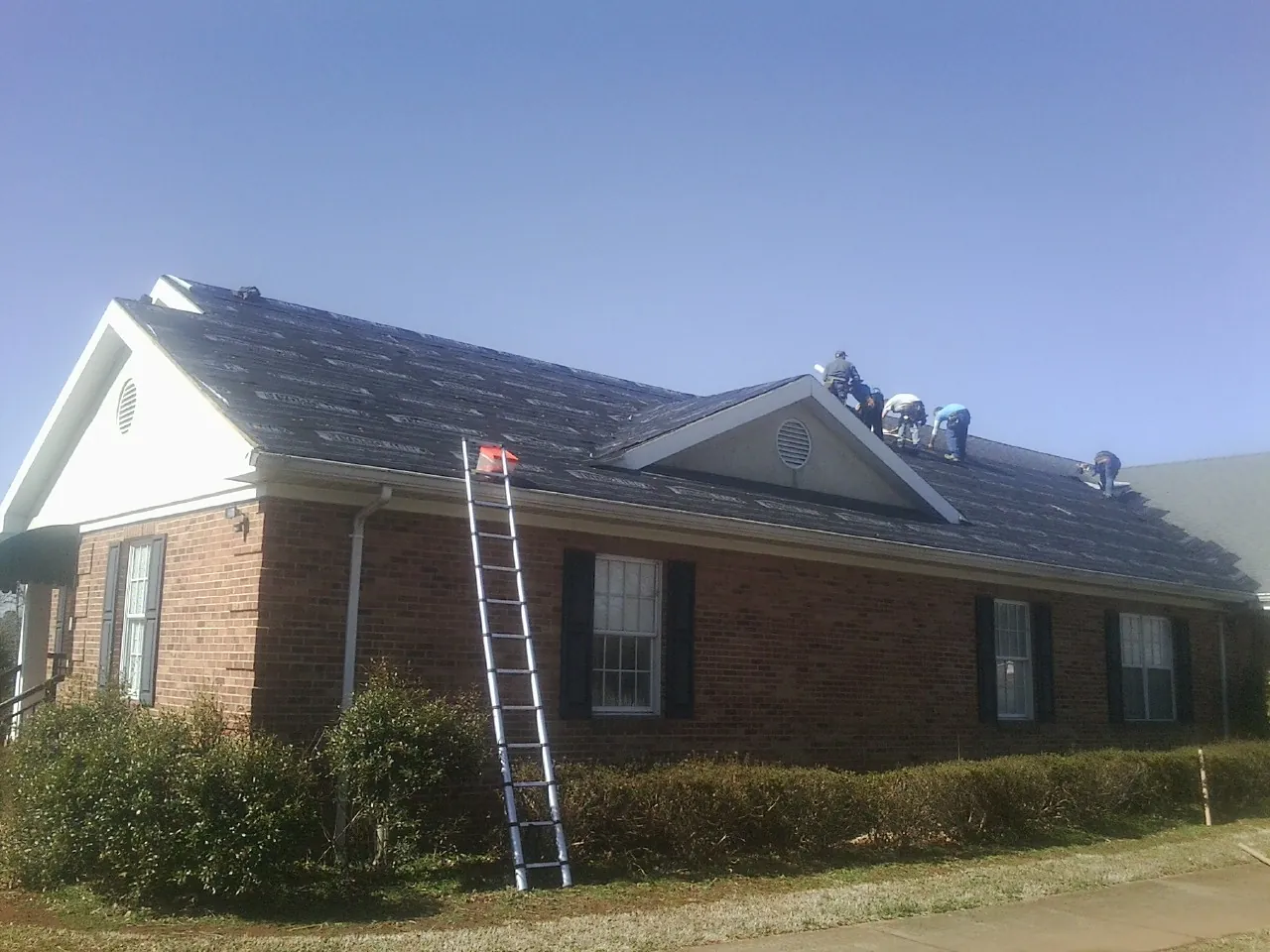 Crew tearing shingles off a brick ranch roof with a ladder set — Emergency Roof Repair work by our crew in Weed
