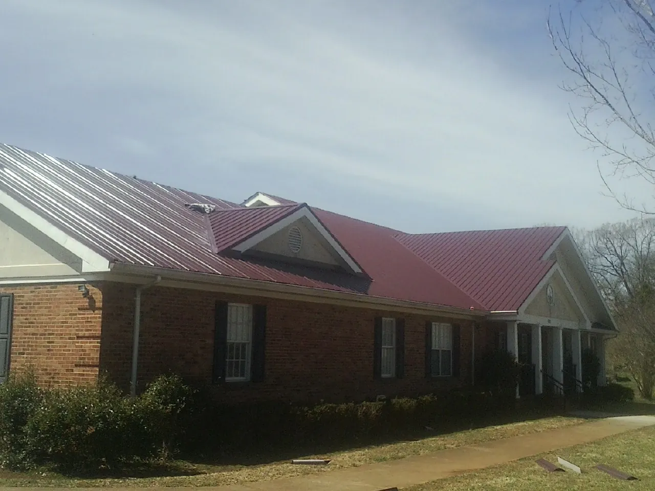Red metal roof with gabled entries on a long brick building, from a Hail Damage Roof Repair job in Weed