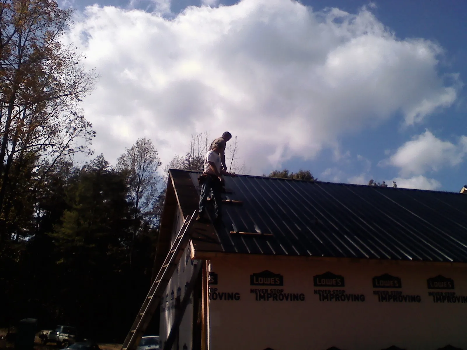 Roofer fastening dark metal panels high against a cloudy sky, from a Roof Inspection job in Weed