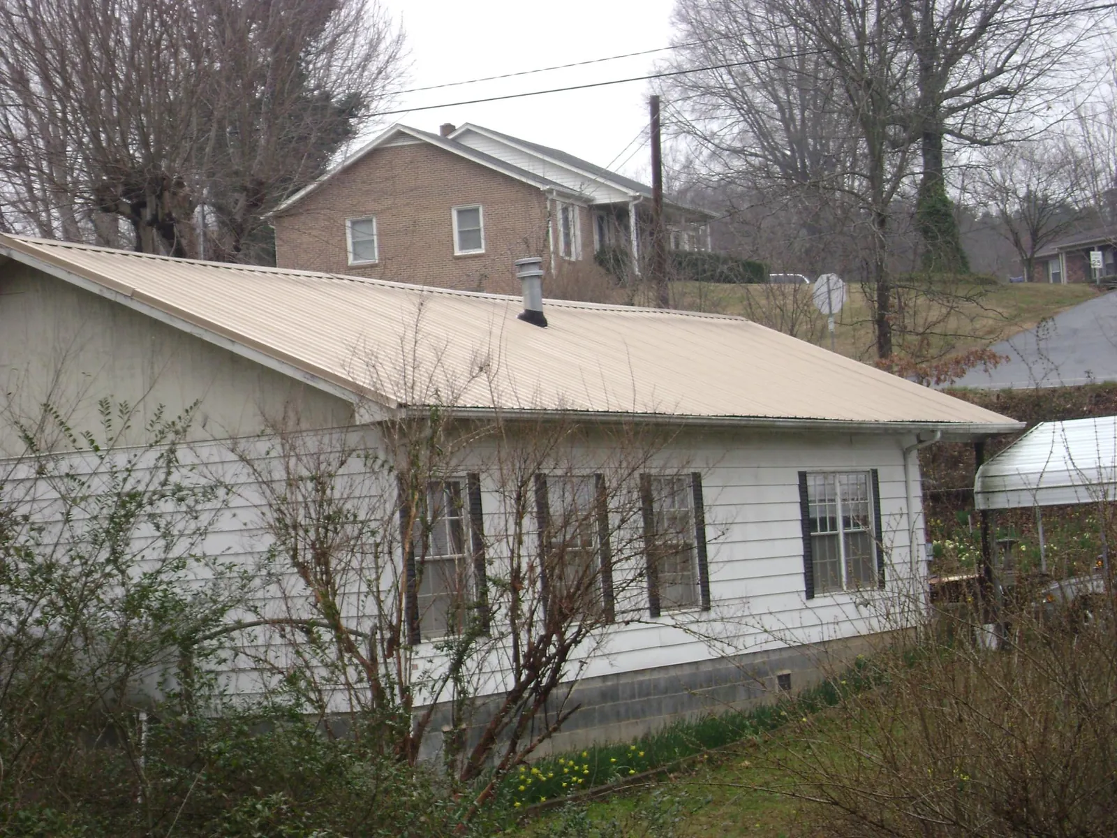 Tan metal roof on a white sided house set into a hillside — Commercial Roofing by Roofing Brothers in Weed